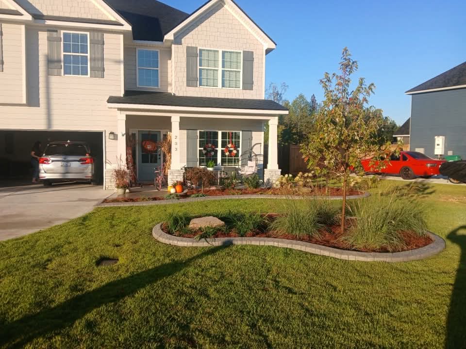 Curved, edged front bed with ornamental grasses, a boulder and fresh mulch
