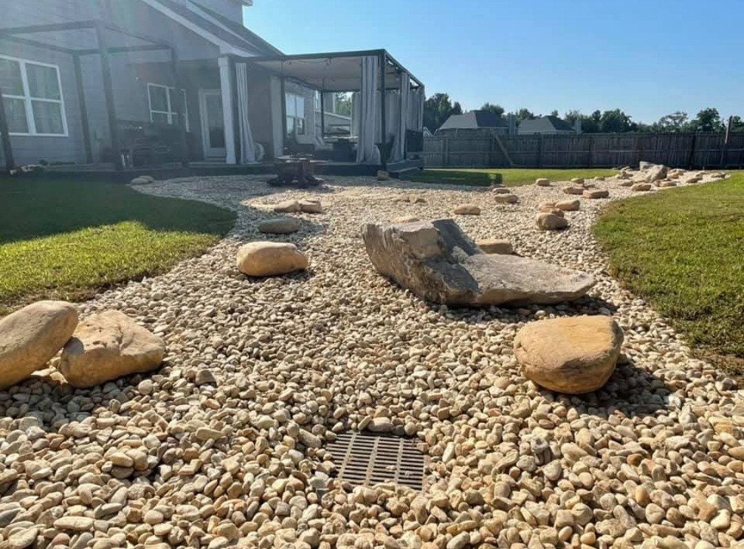 Dry creek bed of river rock and boulders winding through a backyard lawn