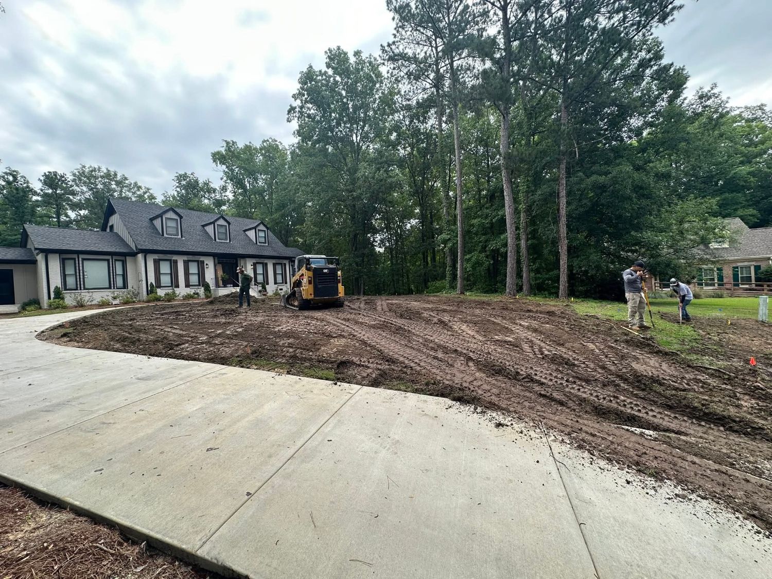 Grade: bare graded dirt in front of the house, with the crew and a CAT track loader