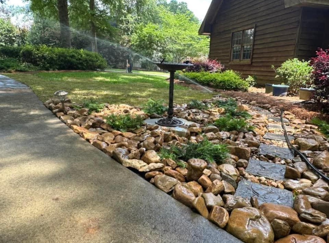 River rock bed with shrubs, stepping stones and a birdbath along a walkway