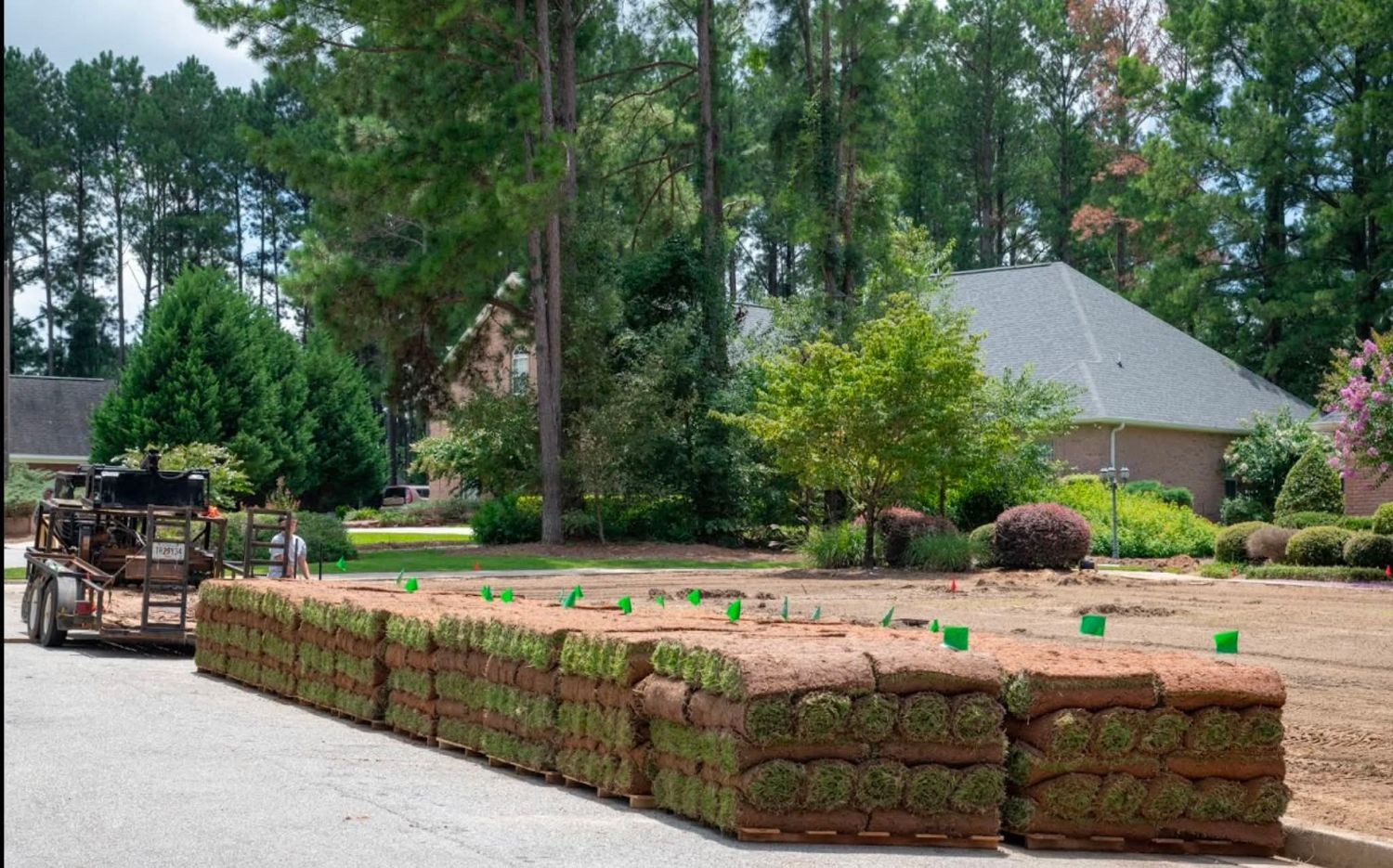 Pallets of fresh sod staged on a graded yard marked with green flags