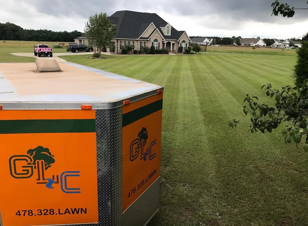 Freshly striped lawn in front of a brick home, seen past the orange GLC trailer