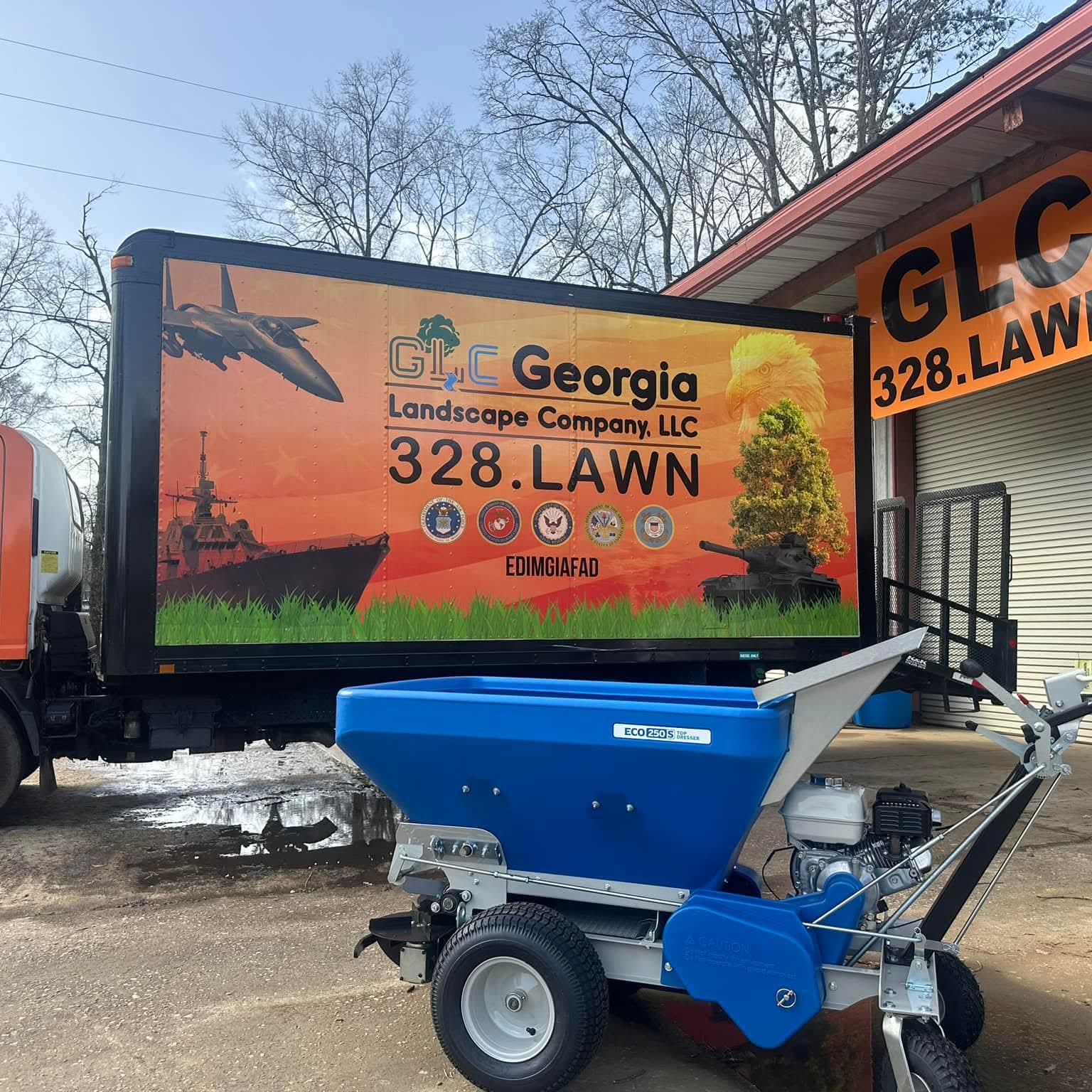 GLC box truck at the shop under the orange GLC 328.LAWN sign, with a new topdresser in front